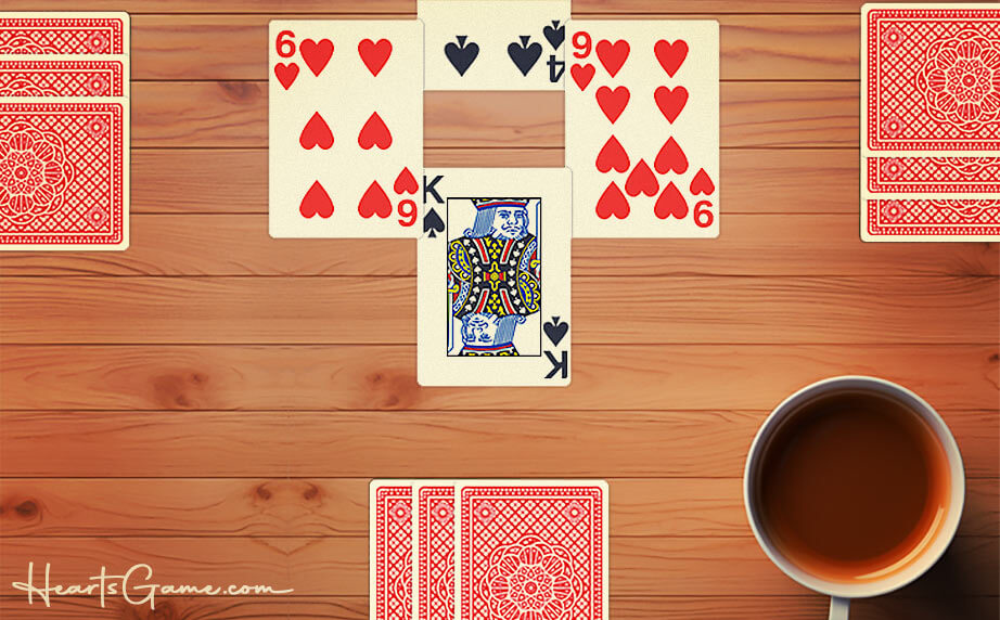 Top view of a Hearts trick-taking card game setup on a wooden table with playing cards laid out